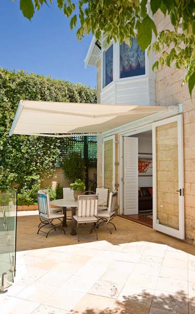 Outdoor living space with cream coloured folding arm awnings on stone house