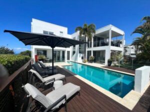 Ultrashade umbrella featured on an outdoor deck with a pool in front of a modern white house