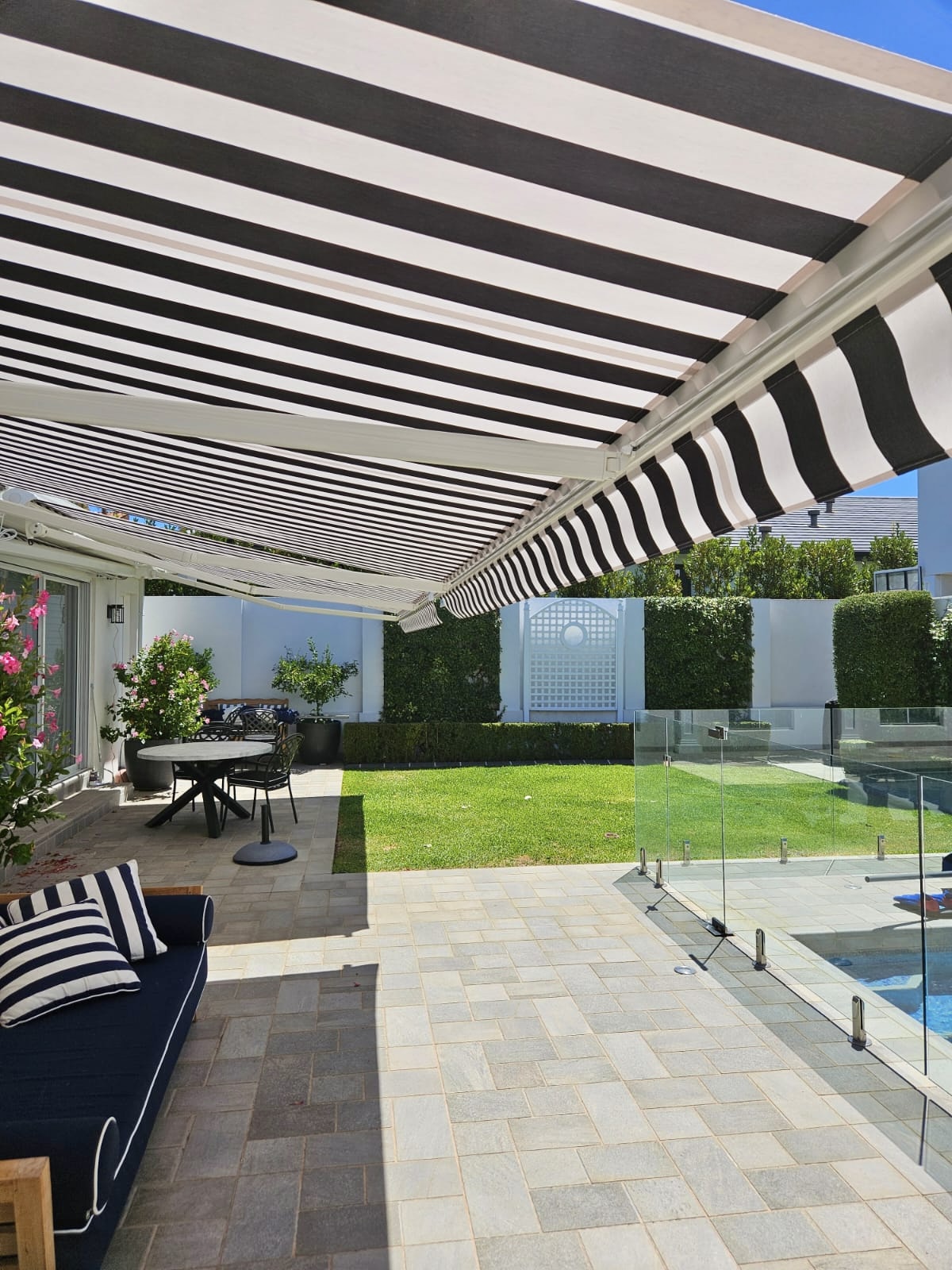 Striped retractable folding arm awning shading an outdoor entertaining area with pool in Perth installed by Kenlow