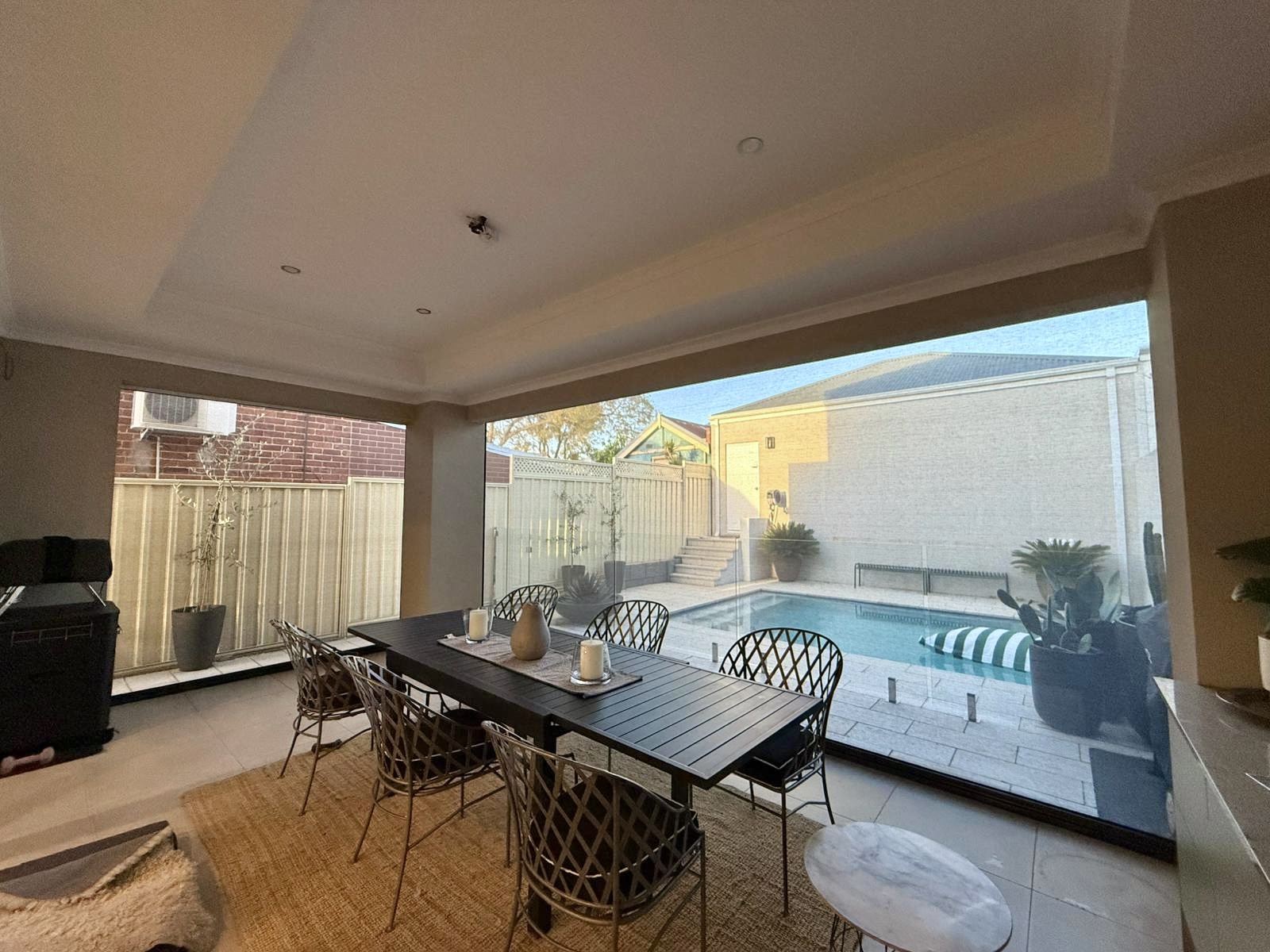 Interior view of a Perth alfresco dining area with Ziptrak blinds retracted, overlooking a glass-fenced swimming pool, installed by Kenlow.