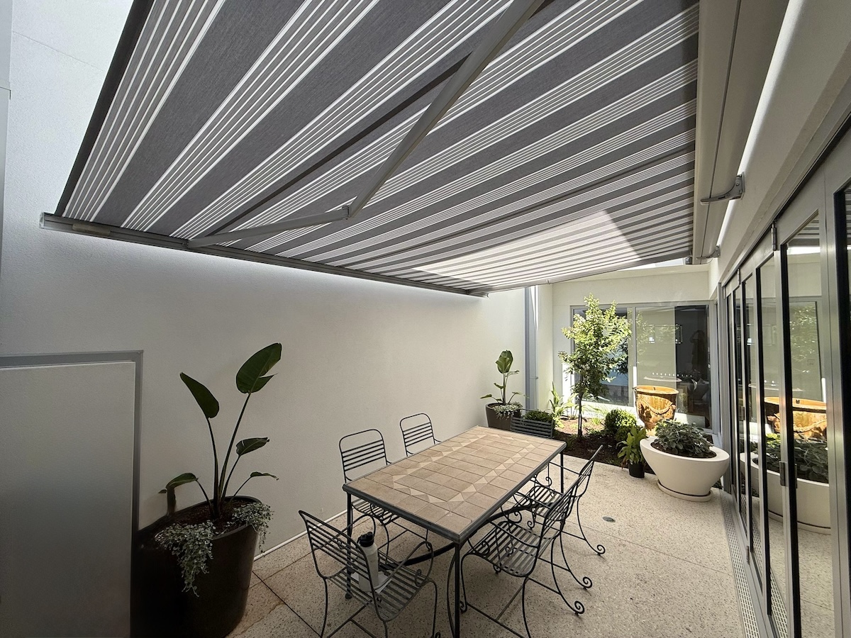 Grey striped folding arm awning shading a courtyard dining table