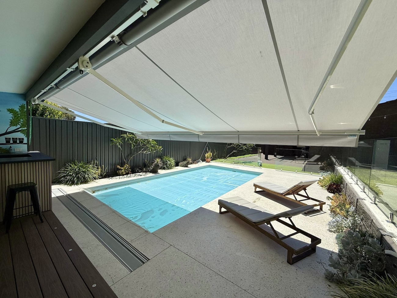 White retractable awning shading poolside sun lounges and a bar area